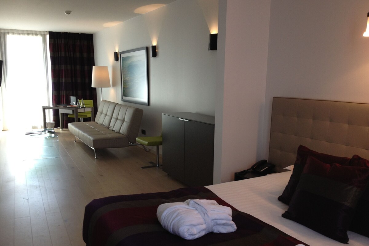 A hotel room with a bed, a sofa, a desk, and a chair.
