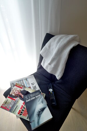 A dark blue sofa with a white towel draped over it, a remote control, and several magazines including one with a cover featuring a woman's face. - Hotel Mercure Villefranche-sur-Saone (Villefranche-sur-Saône)