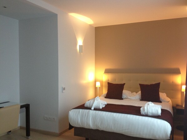 Una habitación de hotel con una cama grande, dos lámparas de noche y un cabecero con panel de luz.