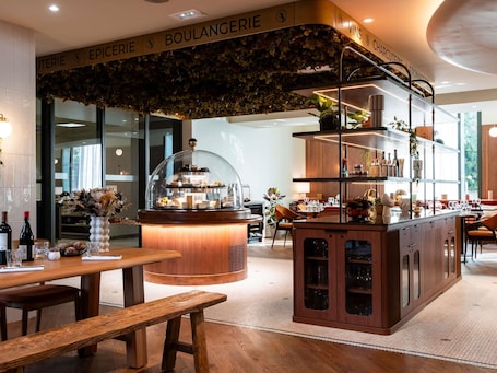 A restaurant with a wooden counter, a glass display case, and a seating area with tables and chairs.. Hotel Mercure Villefranche-sur-Saone