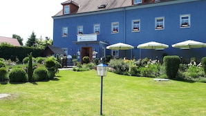 A blue building with a sign reading "Bienvenue & Herzlichen Willkommen" and "L'UBERGE > GUTSCHF." There are three white umbrellas in the front garden. - L' Auberge Gutshof (Bischofswerda)