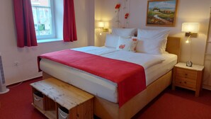A neatly arranged bedroom with a large bed, bedside tables, a nightstand, a wooden bench, a window with curtains, and a wall painting. - L' Auberge Gutshof (Bischofswerda)