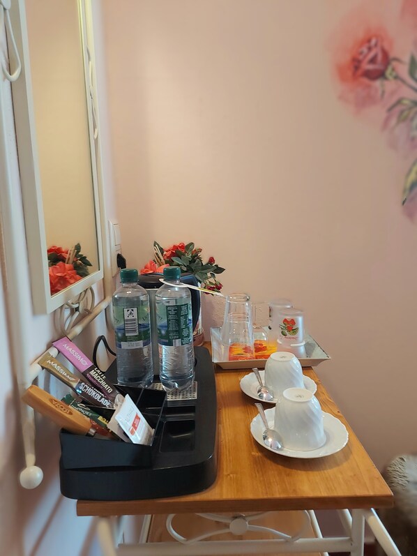 A small table with a water bottle, a box of chocolates, a cup, and a tray with a glass and a candle.