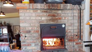 A rustic brick fireplace with a wood-burning stove, a wooden table with a plaid tablecloth, and hanging lights. - L' Auberge Gutshof (Bischofswerda)