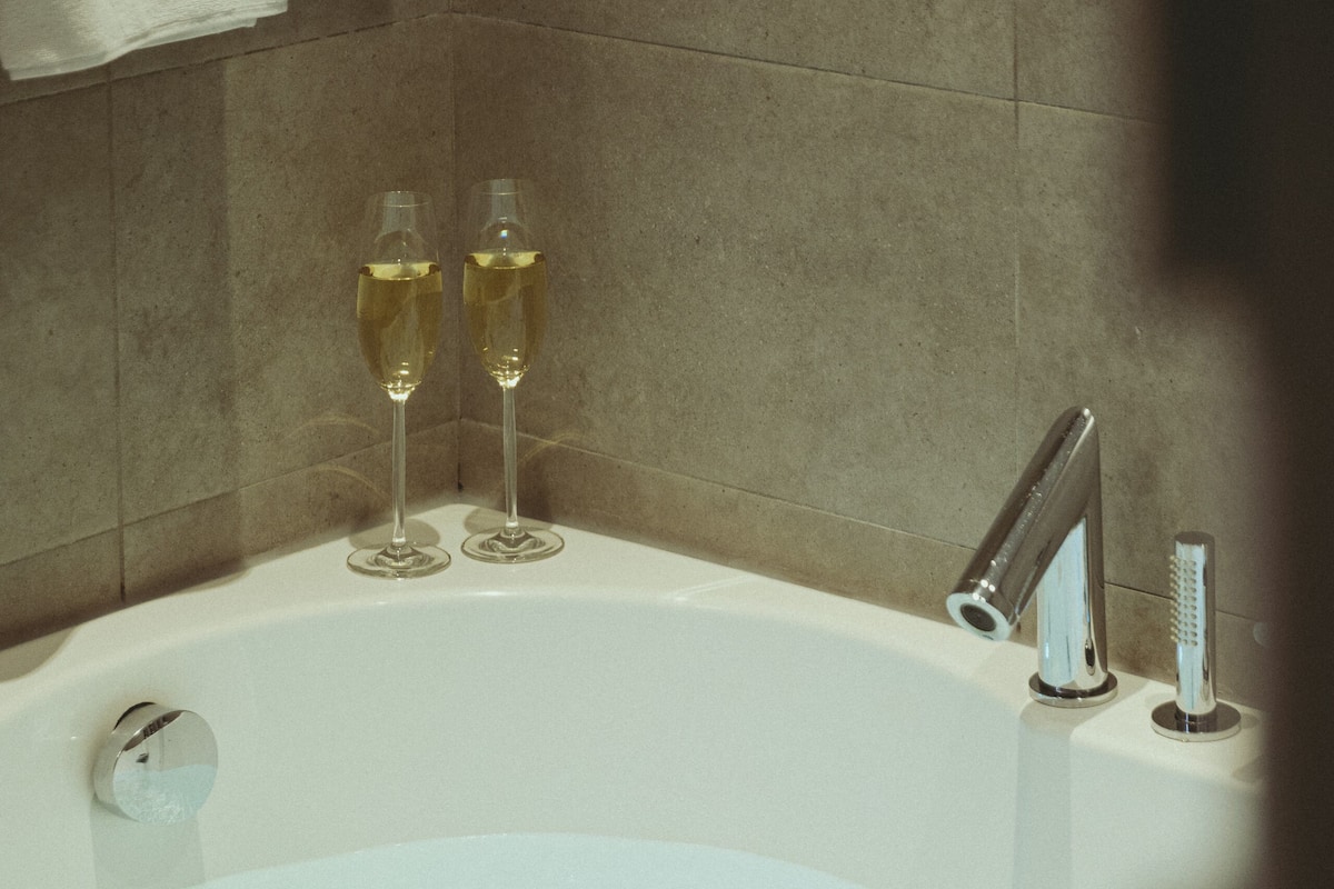 A bathtub with two glasses of champagne, a digital control panel, and a modern faucet.