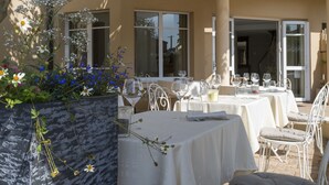 An outdoor dining area with tables and chairs, a planter with flowers, and a covered patio.