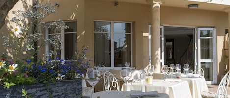 An outdoor dining area with tables and chairs, a planter with flowers, and a covered patio.