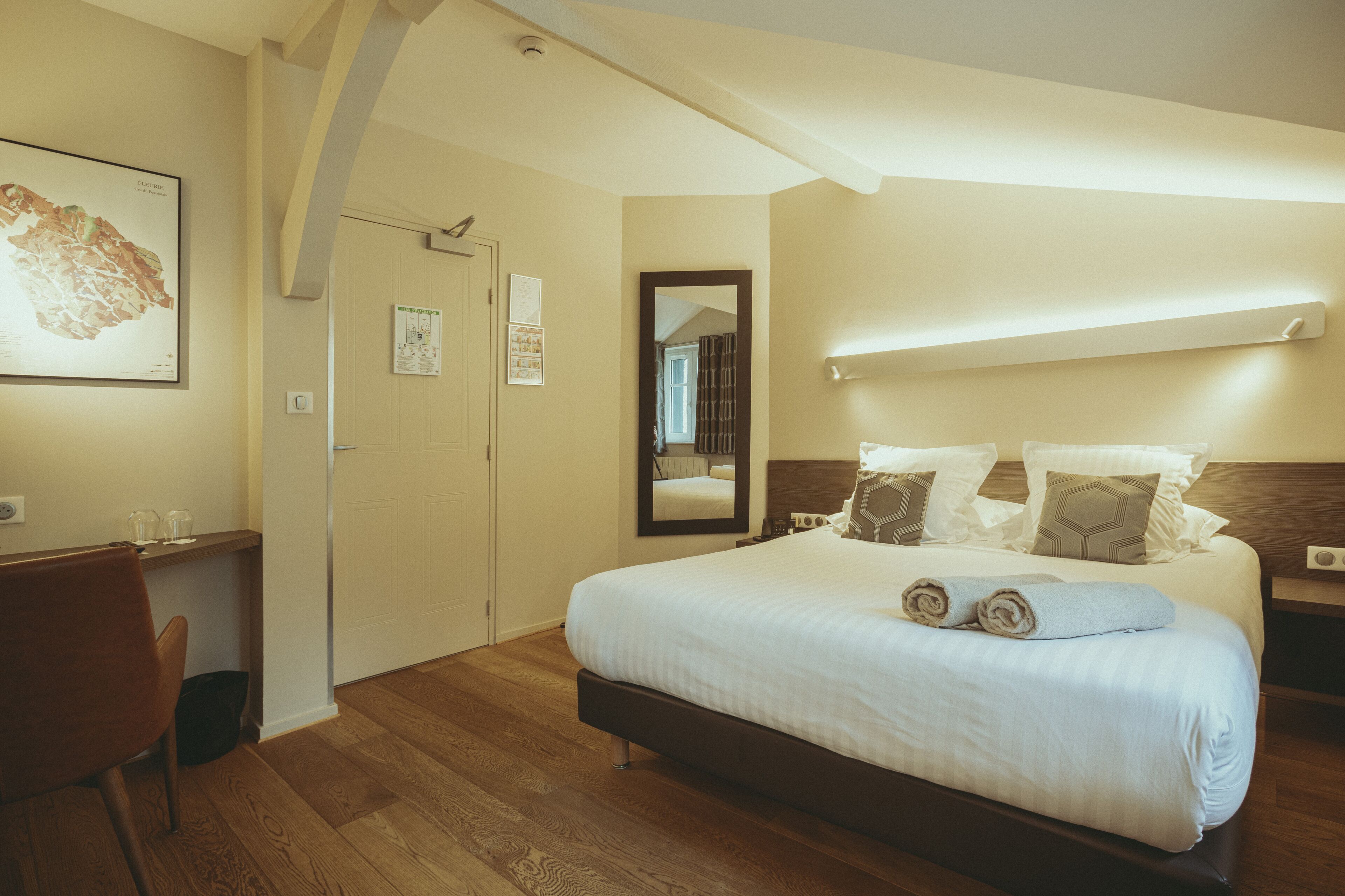 Een slaapkamer met een houten vloer, een bed met wit beddengoed, een bureau met stoel en een kaart aan de muur.