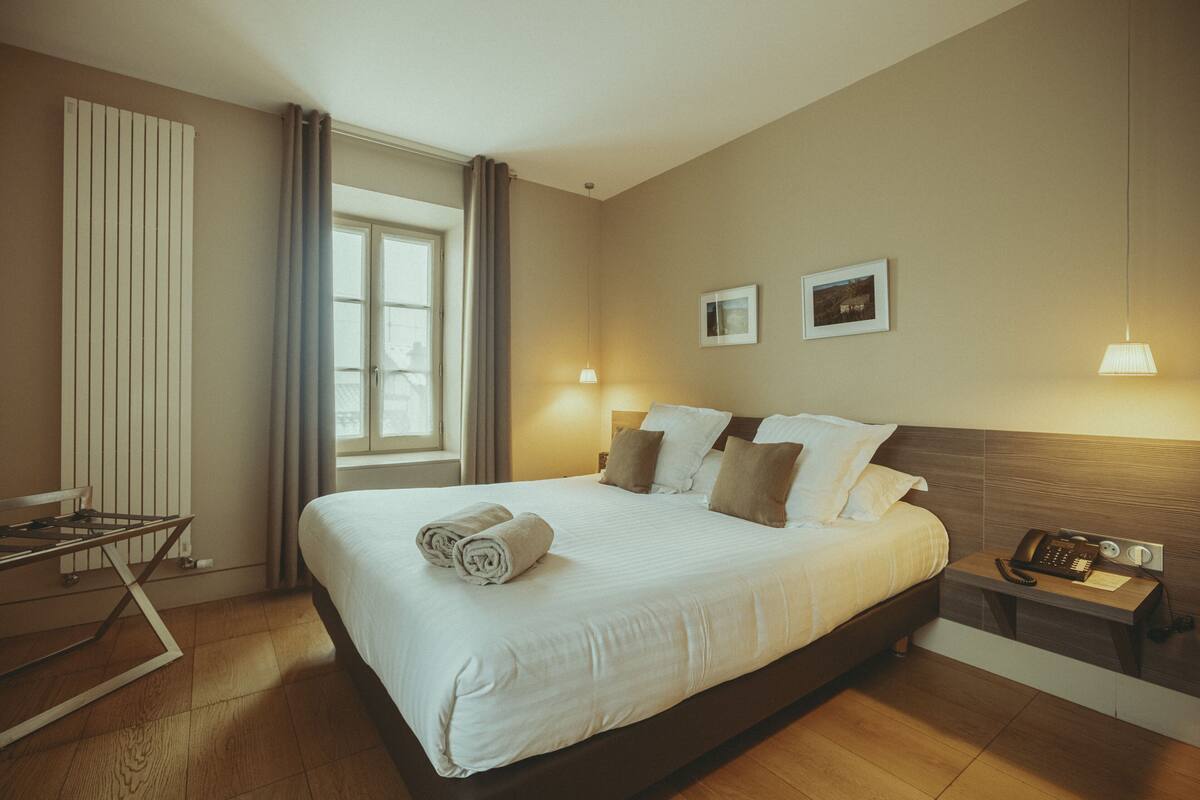 A hotel room with a large bed, bedside lamps, a telephone, and a window with curtains.