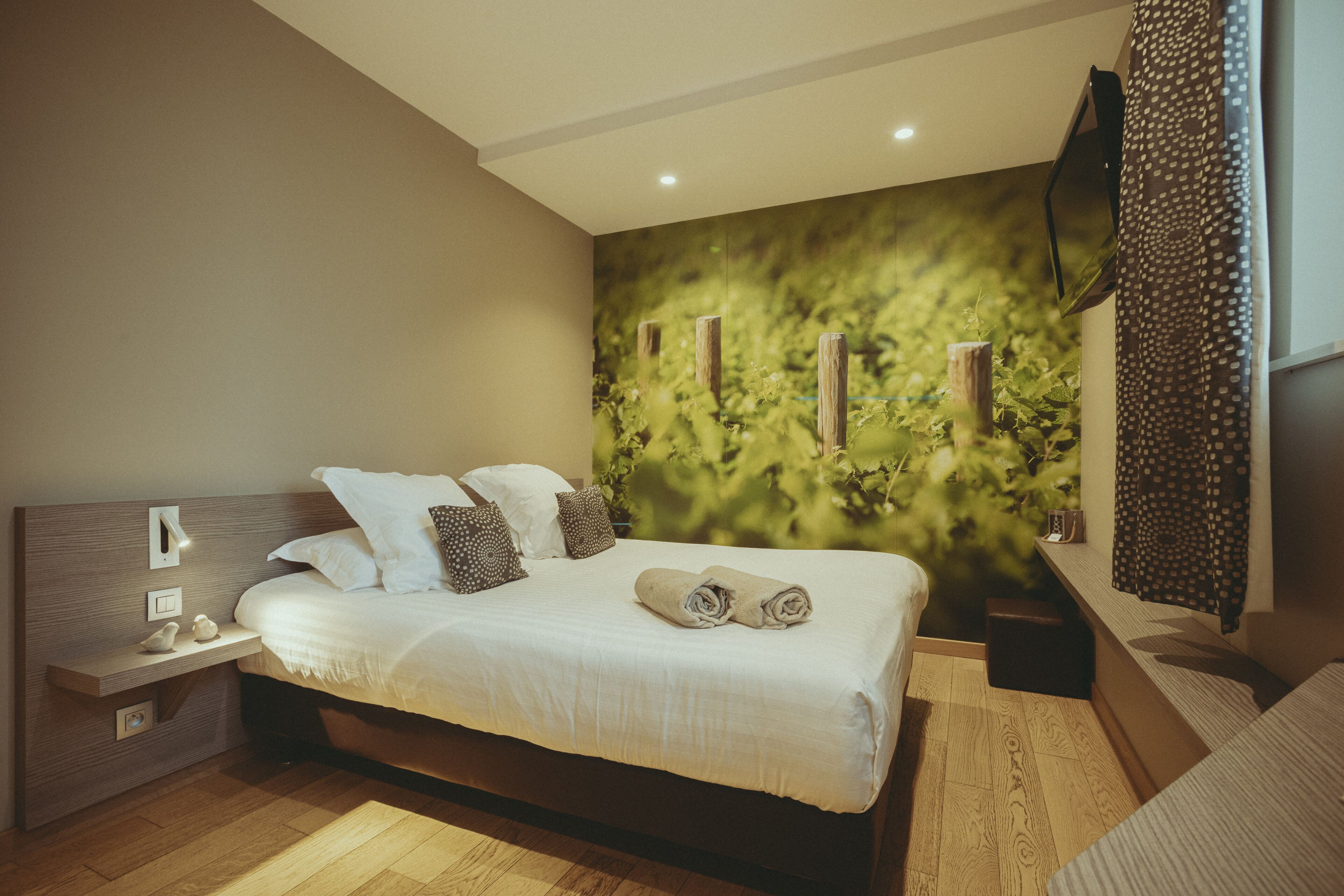 Une chambre moderne avec un grand lit, une table de chevet, un téléviseur fixé au mur et un mur vert à texture.