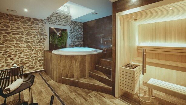 A modern bathroom with a stone wall, a wooden bathtub, and a sauna area.
