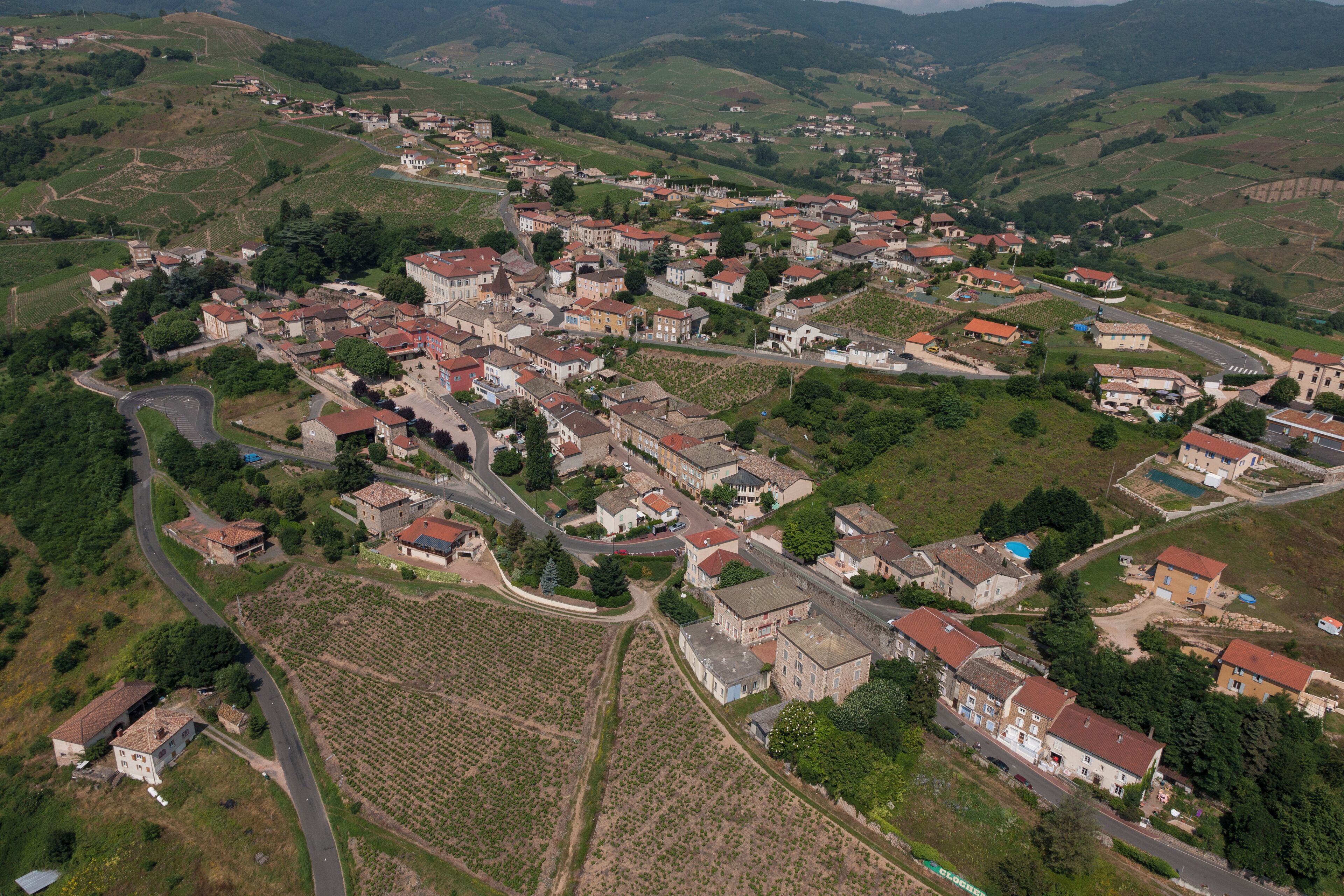 Un village rural doté d’une place centrale, bordée de maisons et de vignobles.