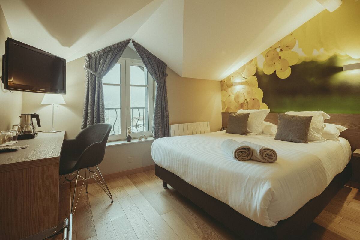 A hotel room with a bed, a desk, a chair, a TV, and a window with curtains.