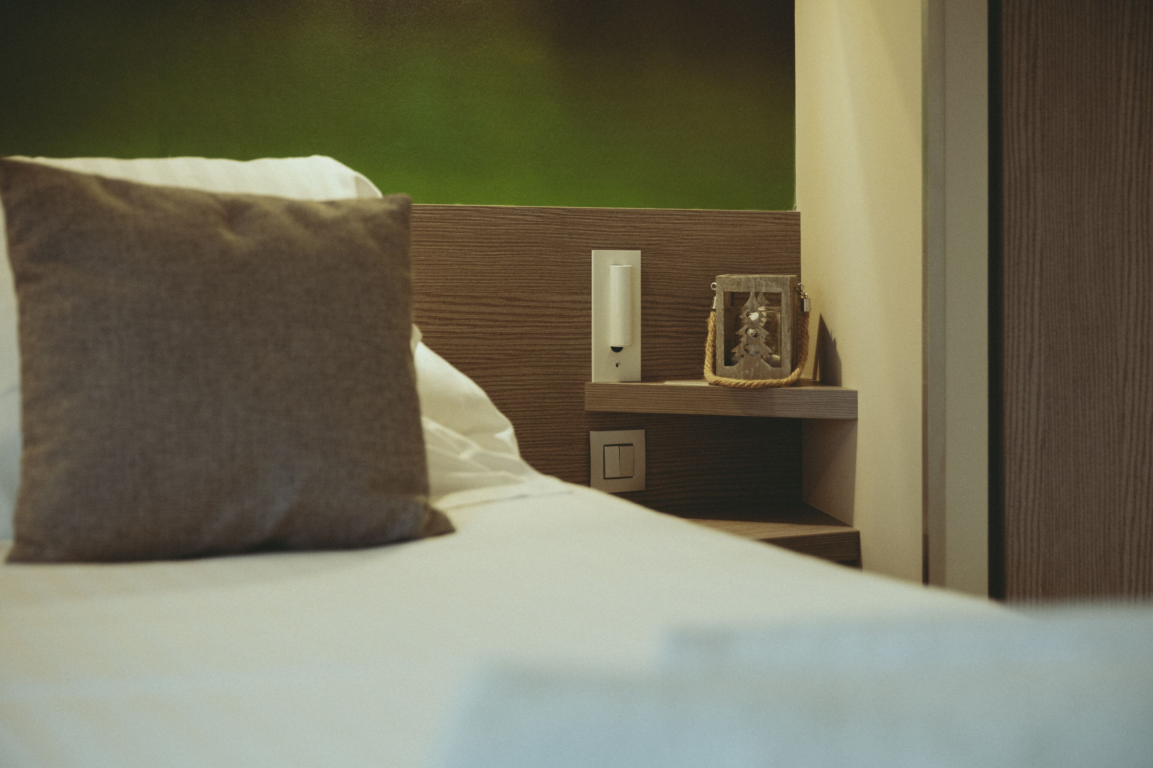 A neatly made bed with a pillow and a bedside table with a framed picture and a switch.