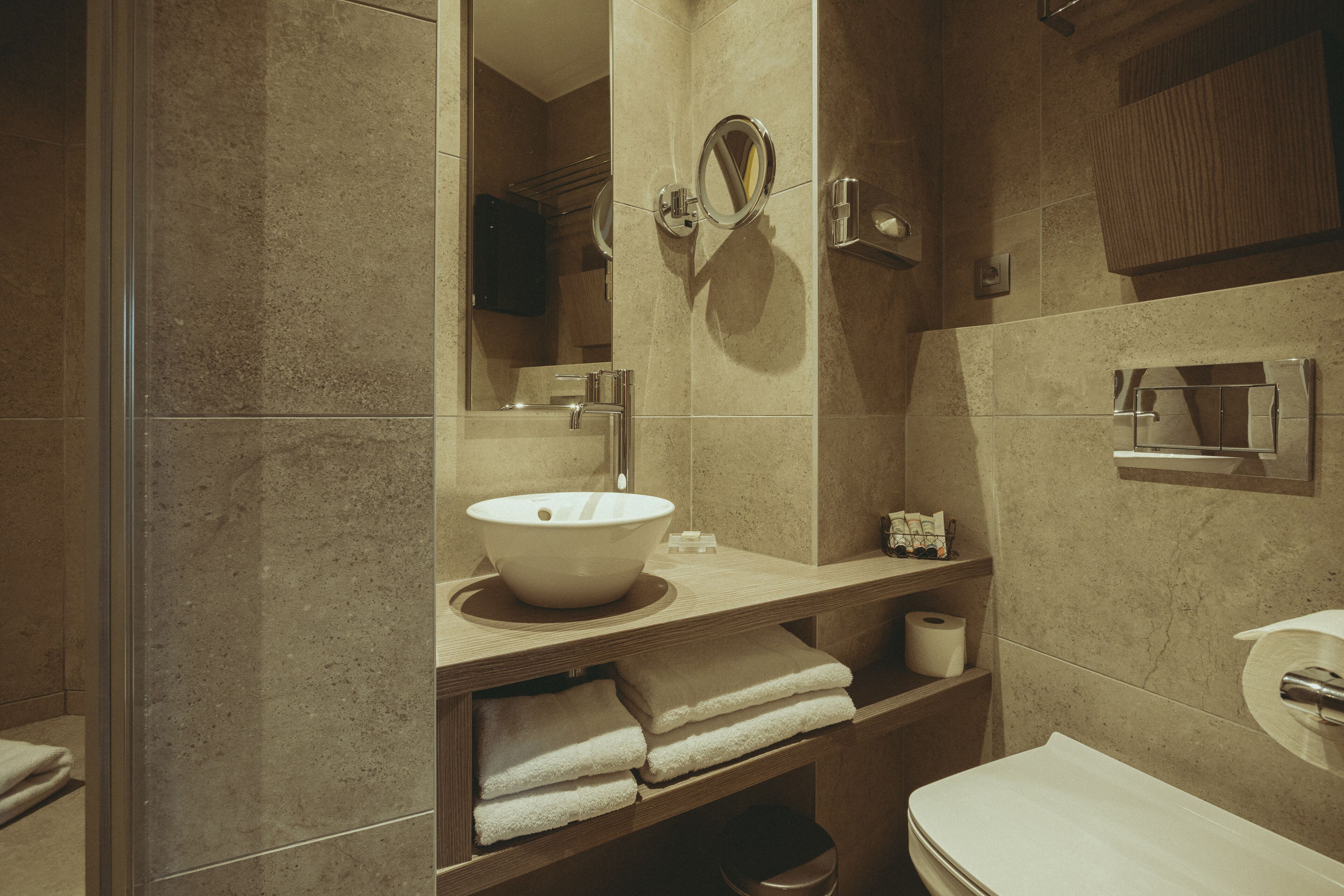 A bathroom with a large mirror, a sink, and a toilet. There are towels and a soap dispenser on the counter.