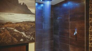 A modern bathroom with a large shower, a stone wall, and a scenic mural of a coastal landscape.