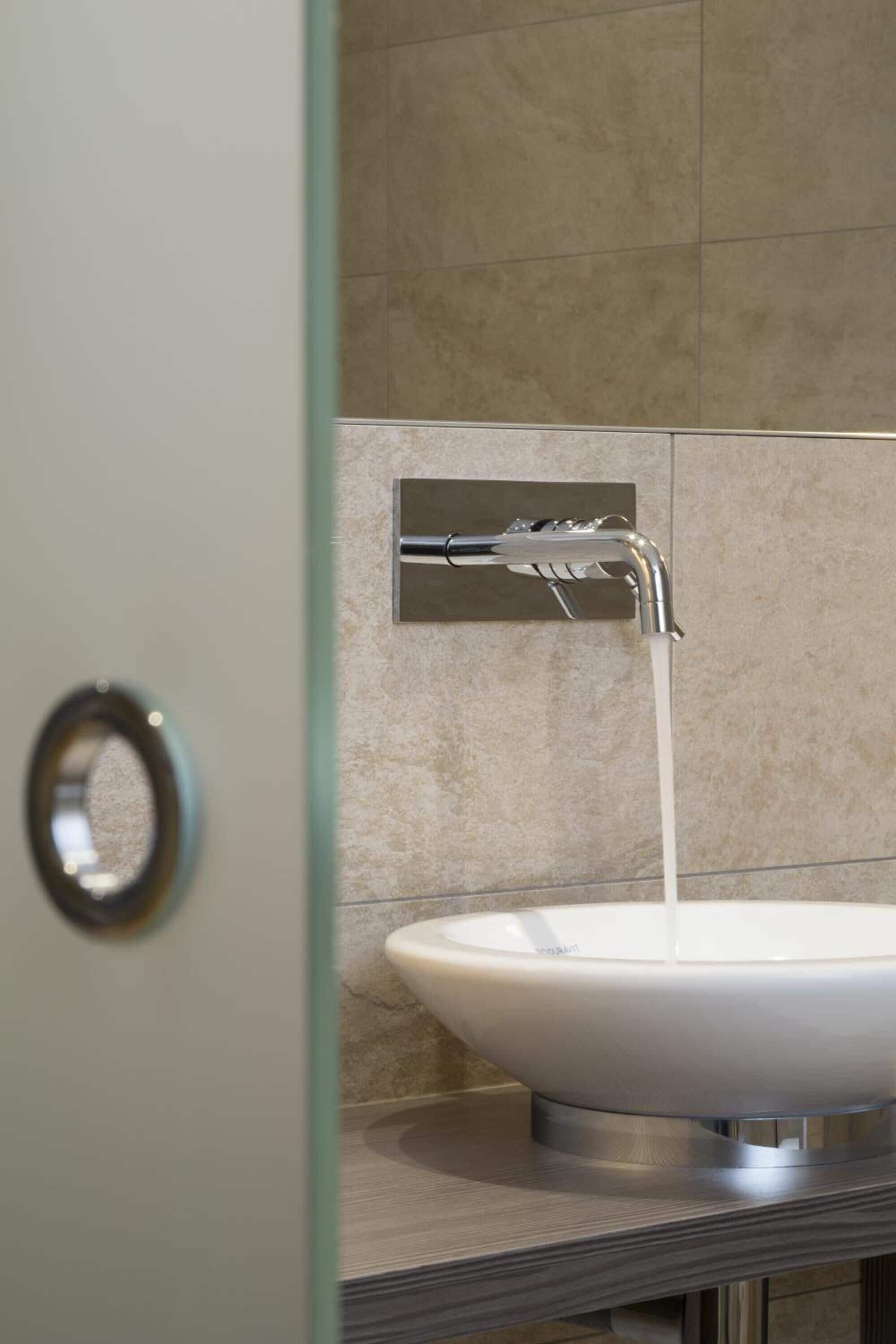 Un baño con un lavamanos blanco, un grifo de cromo y paredes con azulejos color beige.