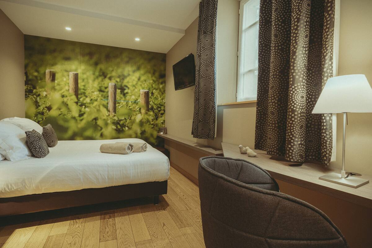 A bedroom with a bed, a chair, a TV, and a window with curtains.