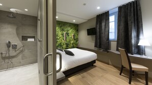 A modern hotel room with a shower, a bed, a desk, and a TV.
