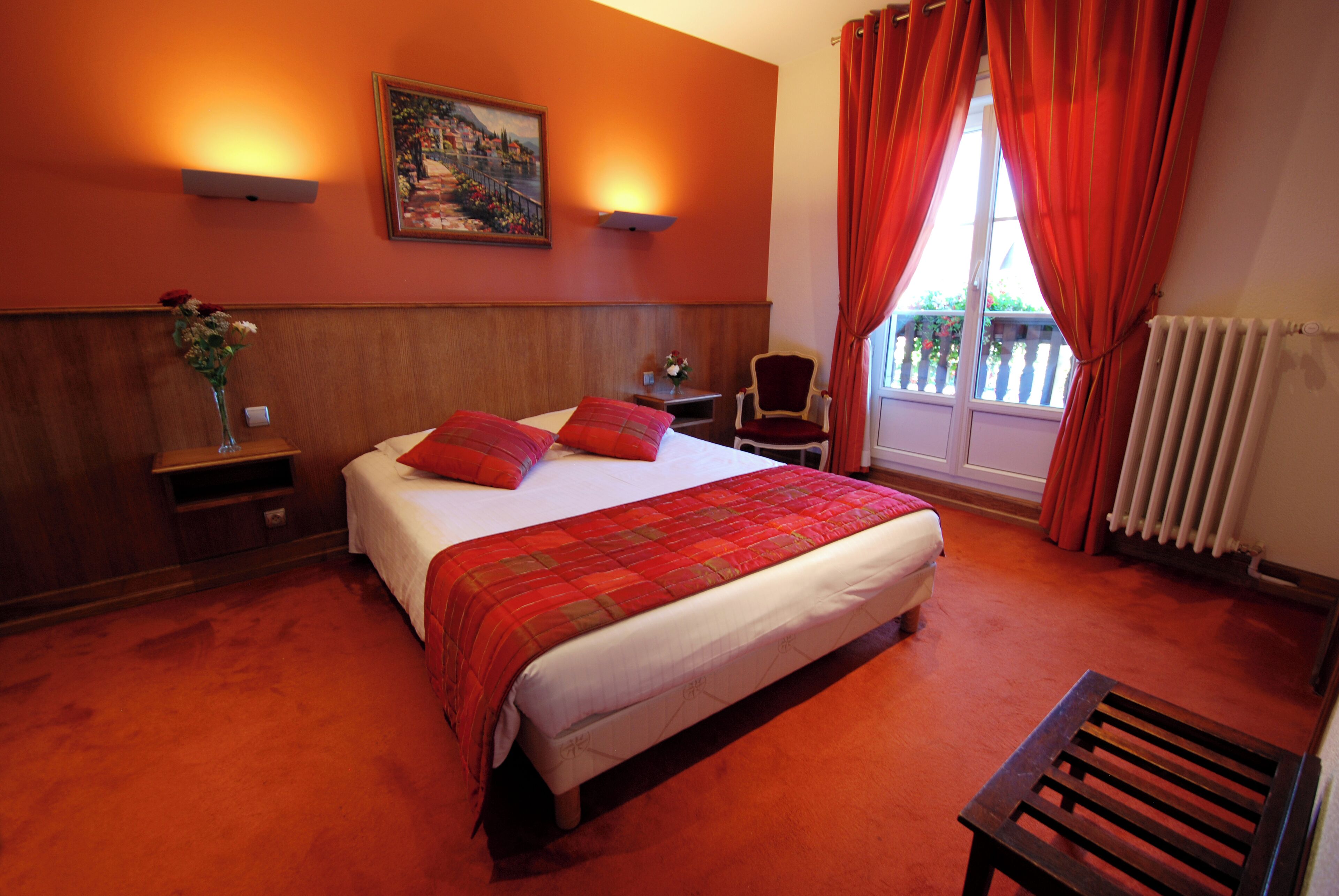 A hotel room with a large bed, a chair, a small table, and a window with curtains.