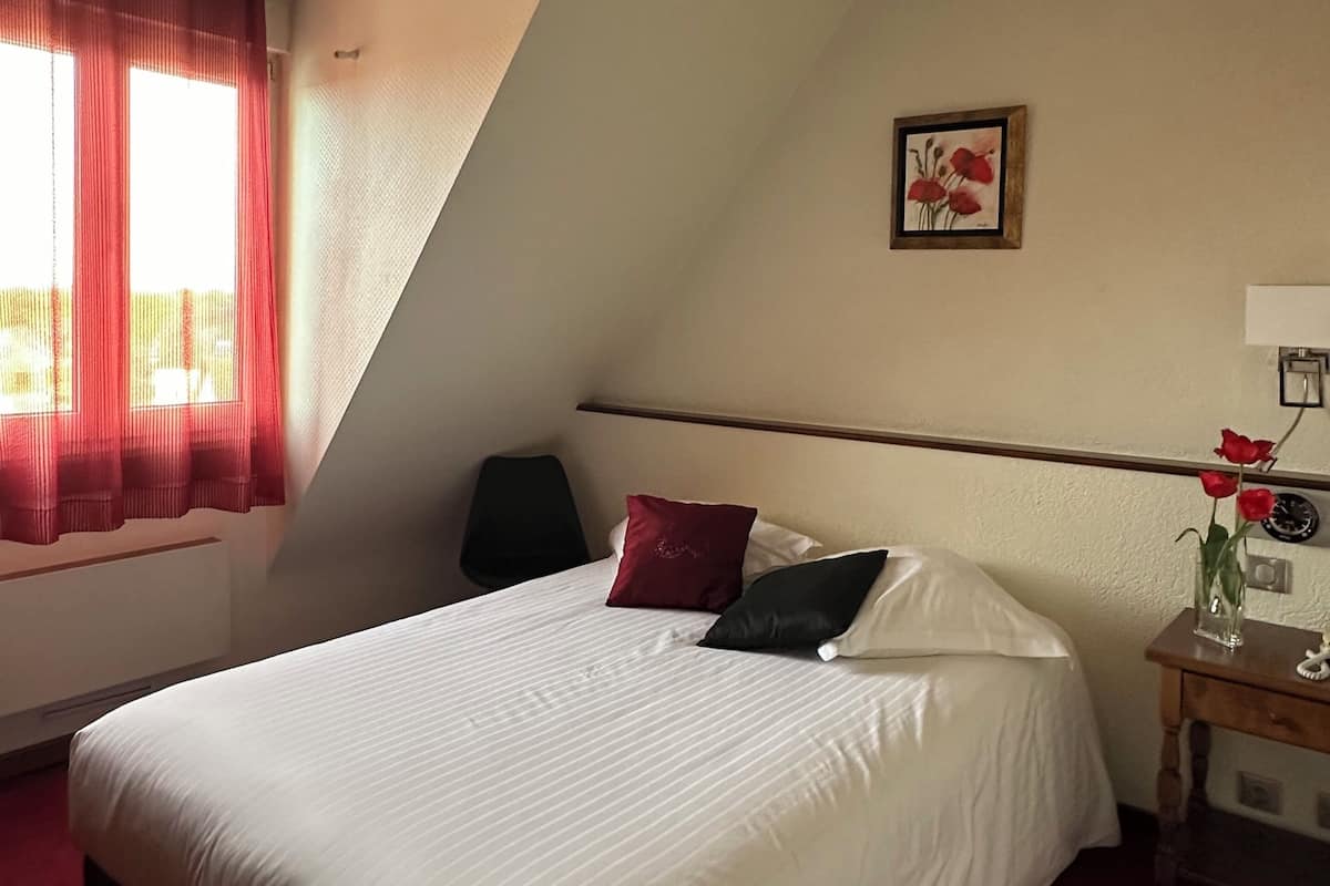 Ein Hotelzimmer mit einem großen Bett, einem Nachttisch, einem roten Vorhang und einem Gemälde an der Wand.