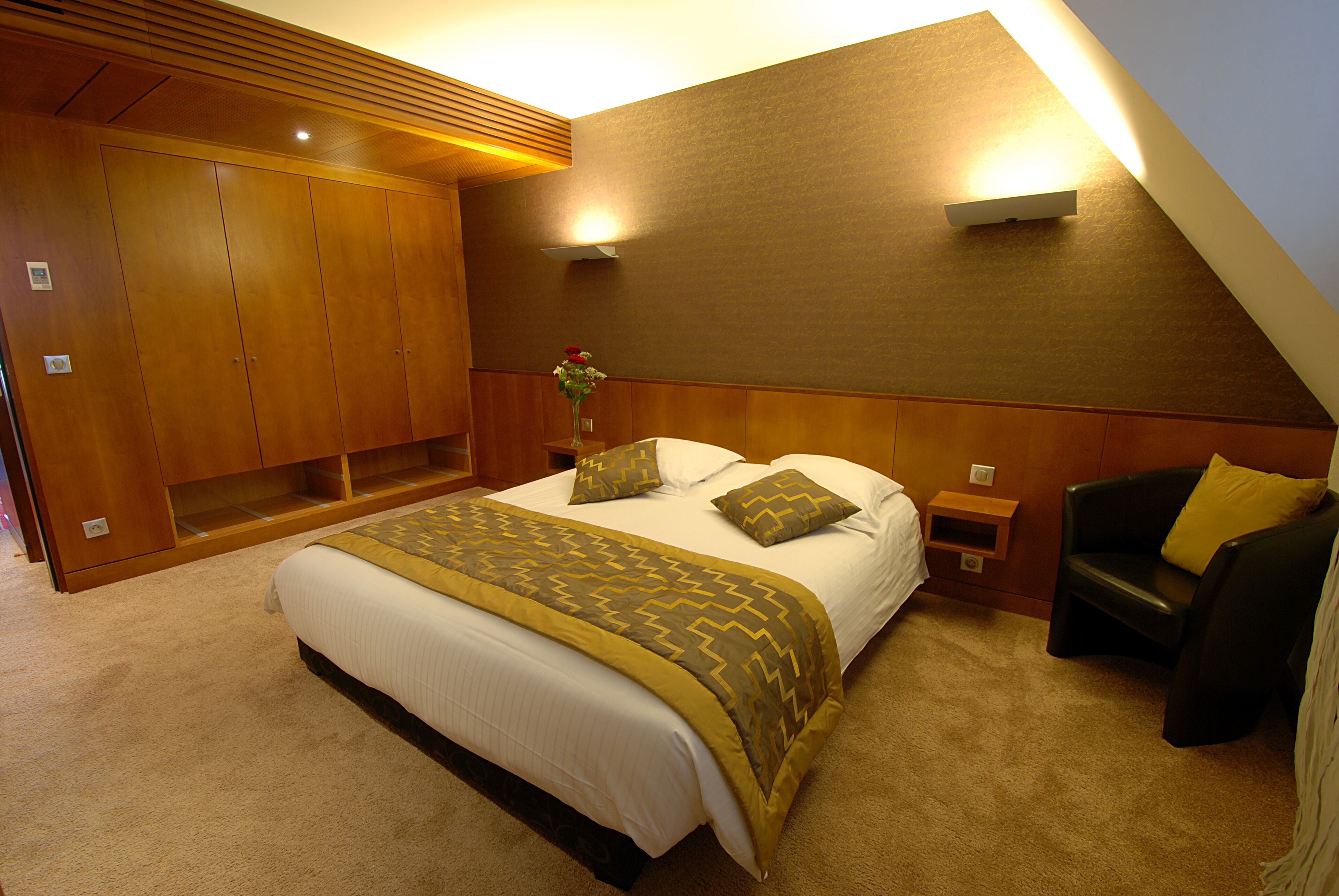 A bedroom with a large bed, a nightstand, a chair, and a wooden wardrobe.