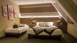 A hotel room with two beds, a large window with blinds, a staircase, and artwork on the wall.
