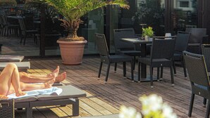 An outdoor patio area with a seating arrangement, a potted plant, and a view of the building in the background.