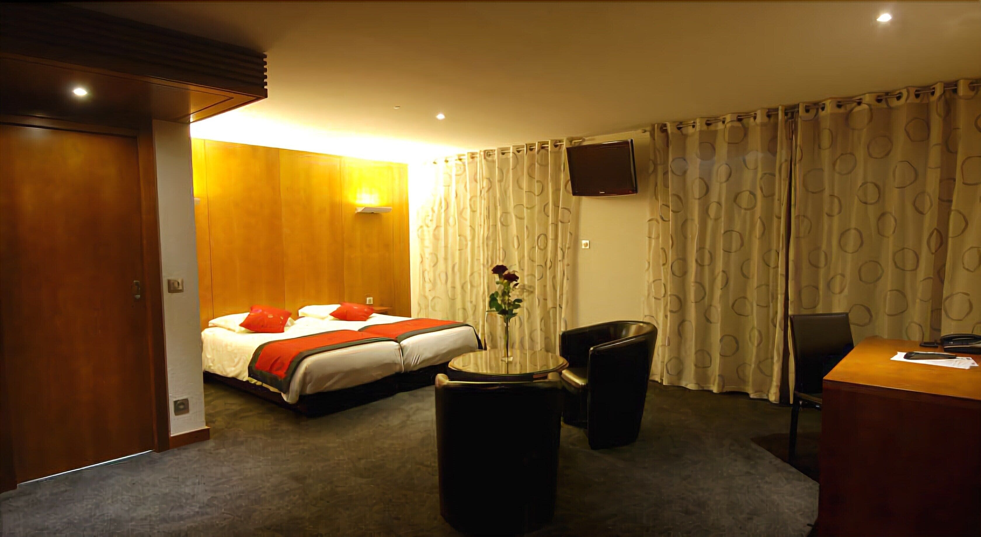 A hotel room with a bed, a desk, a chair, a small table, and a TV on the wall.