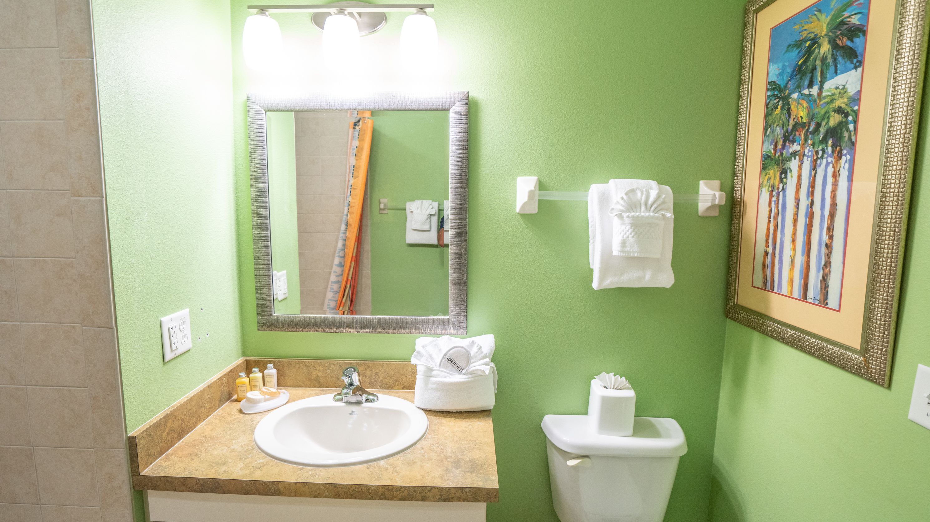 A bathroom with a sink, mirror, toilet, and a framed painting on the wall.