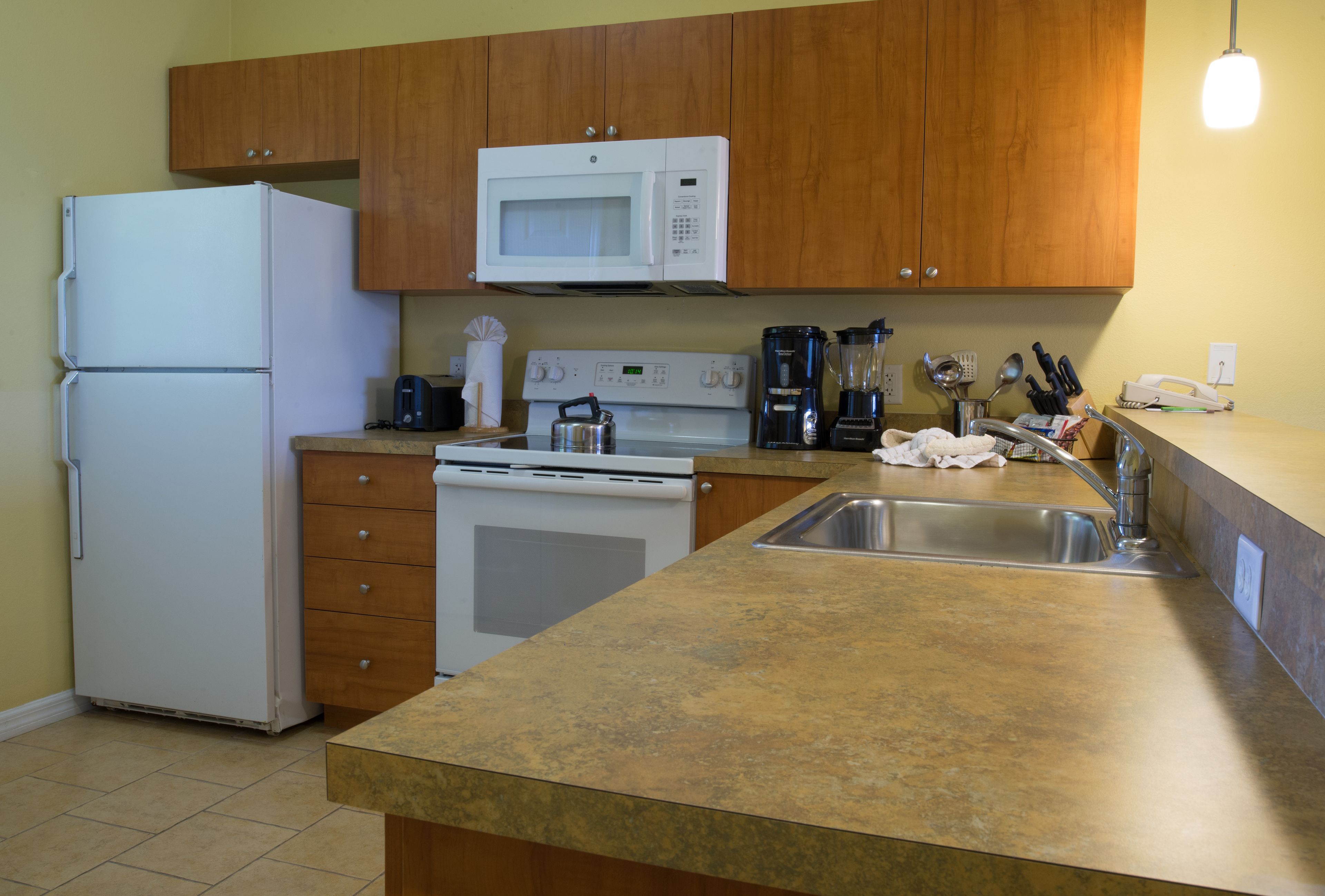 A kitchen with wooden cabinets, a white refrigerator, a microwave, a stove, a coffee maker, and a sink.