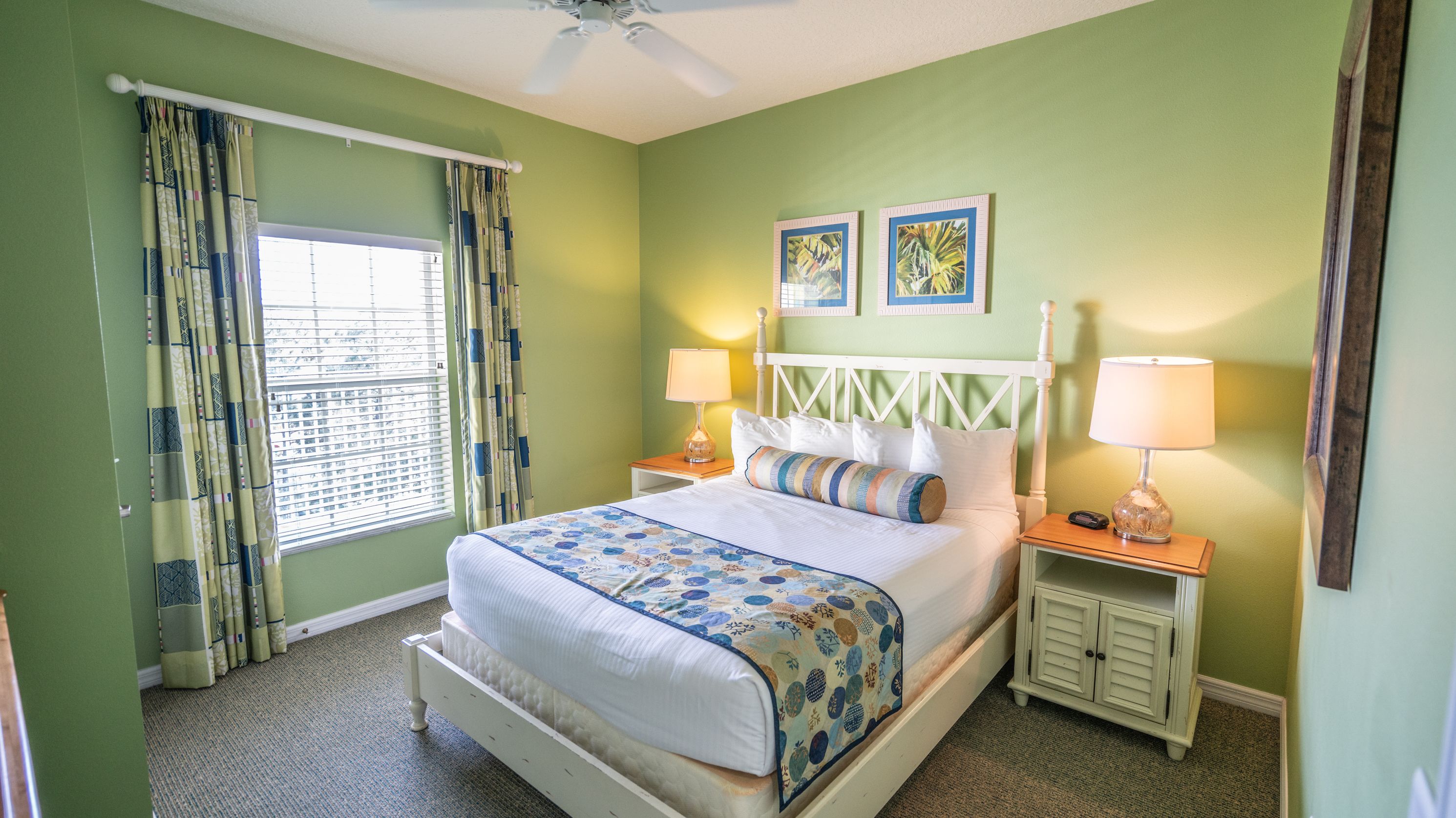 A neatly made bed with a floral bedspread, two bedside lamps, and a window with curtains.