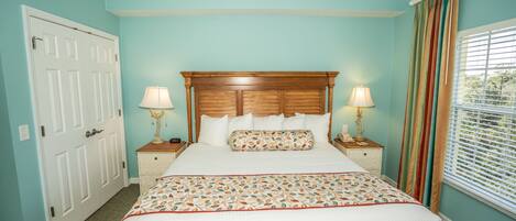 A bedroom with a large bed, two bedside tables with lamps, a wooden headboard, and a window with blinds.