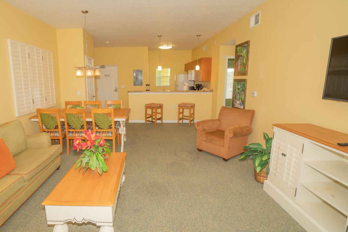 A living room with a sofa, coffee table, and chairs, a kitchen area with a dining table and chairs, and a small cabinet.
