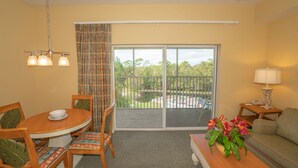 Ein Zimmer mit Esstisch, Stühlen, einer Couch, einer Lampe und Blick auf einen Pool und Grünflächen durch eine Schiebetür.