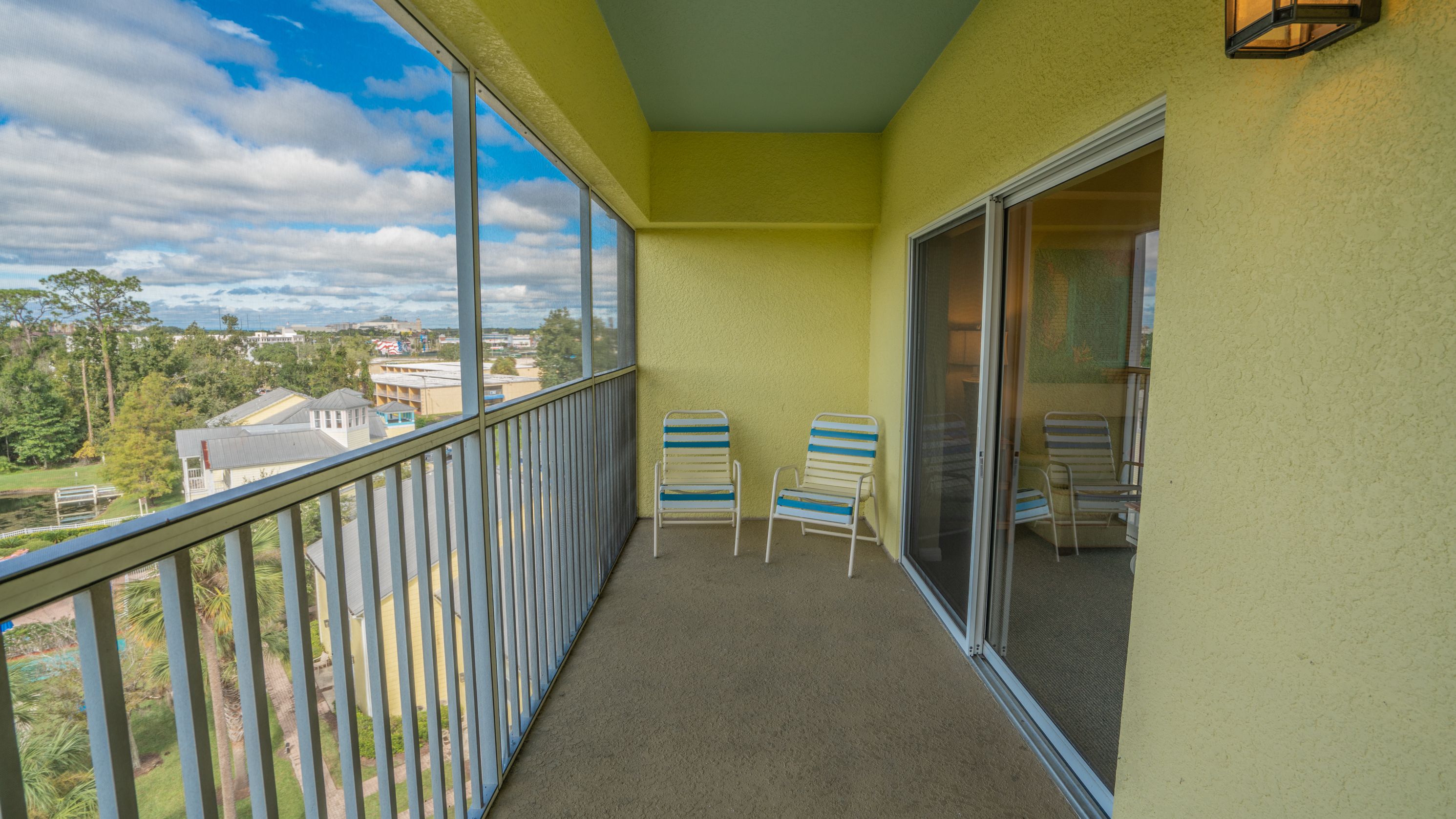 A balcony with a view of the city, two striped chairs, and a sliding glass door.