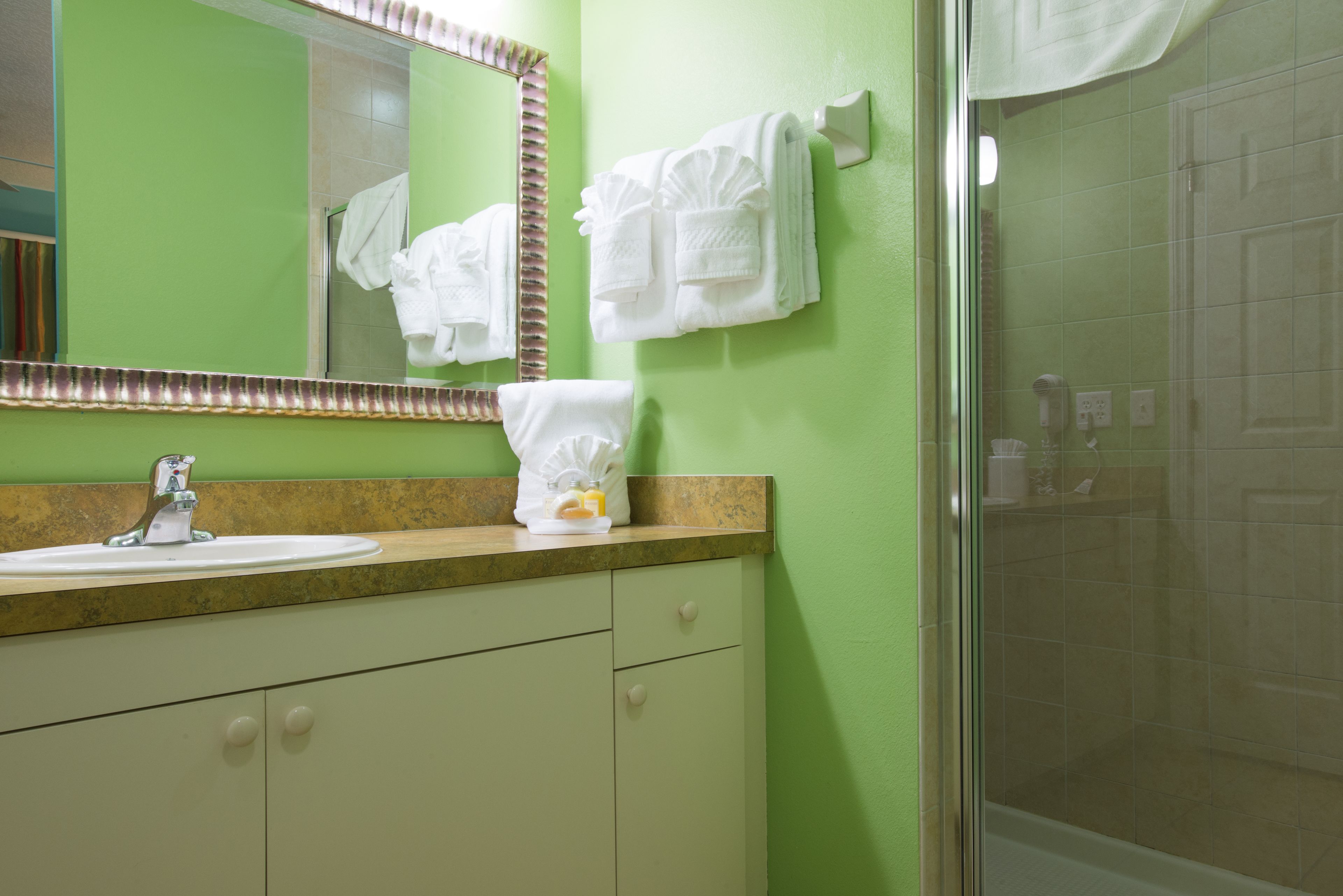 A bathroom with a green wall, a sink with a mirror, and a shower area.