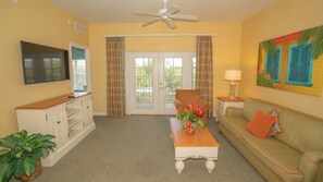 A living room with a television, a sofa, a coffee table, a chair, and a window with curtains. - Barefoot Suites (Kissimmee)