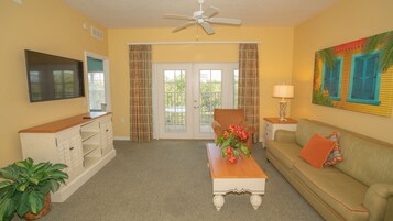 A living room with a television, a sofa, a coffee table, a chair, and a window with curtains.