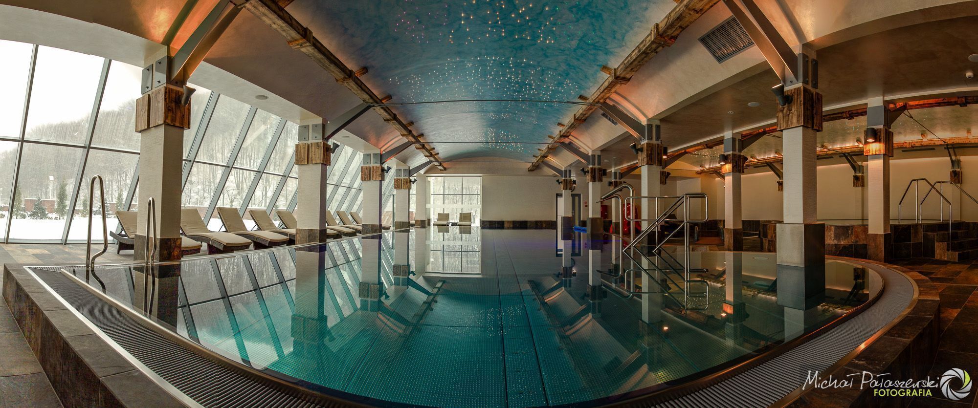 A large indoor swimming pool with a glass barrier, wooden beams, and a ceiling with a starry design.
