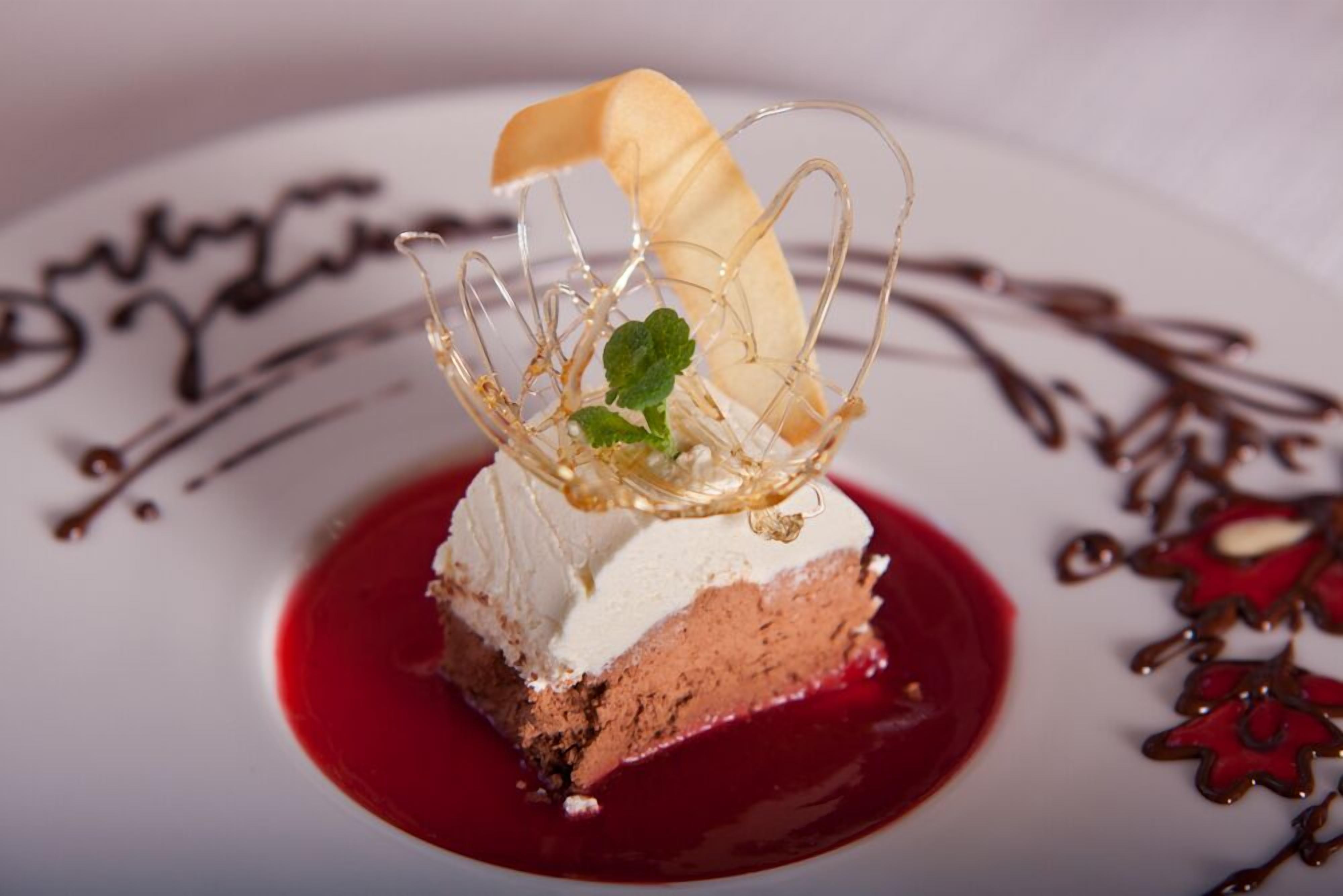 Postre amb una clareda de vidre i fulles de menta sobre un plat amb salsa vermella.