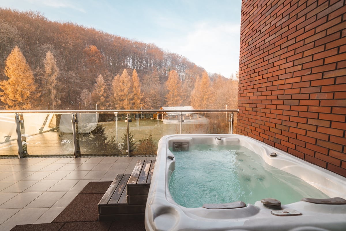 Un jacuzzi en un balcón con vistas a una ladera boscosa.