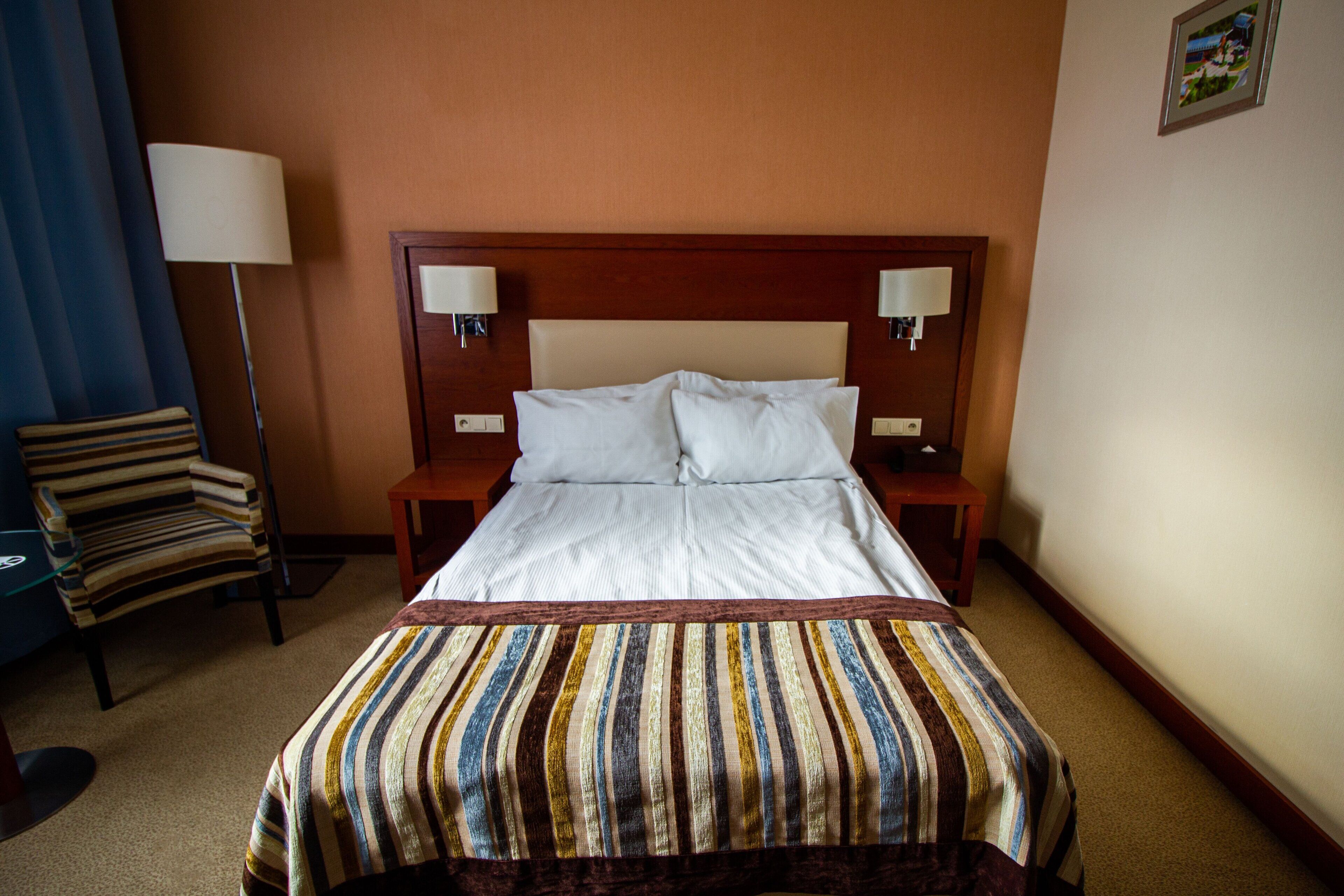 Habitación de hotel con una cama grande, dos lámparas de noche, una manta a rayas, una silla a rayas y una lámpara de pie.