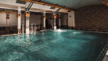 An indoor swimming pool with clear water, wooden beams on the ceiling, and a stone wall on one side.