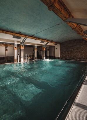 An indoor swimming pool with clear water, wooden beams on the ceiling, and a stone wall on one side. - Mlyn Jacka Hotel & Spa (Wadowice)