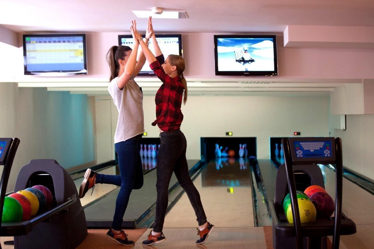 A bowling alley with multiple lanes, bowling balls, and overhead screens displaying bowling animations.