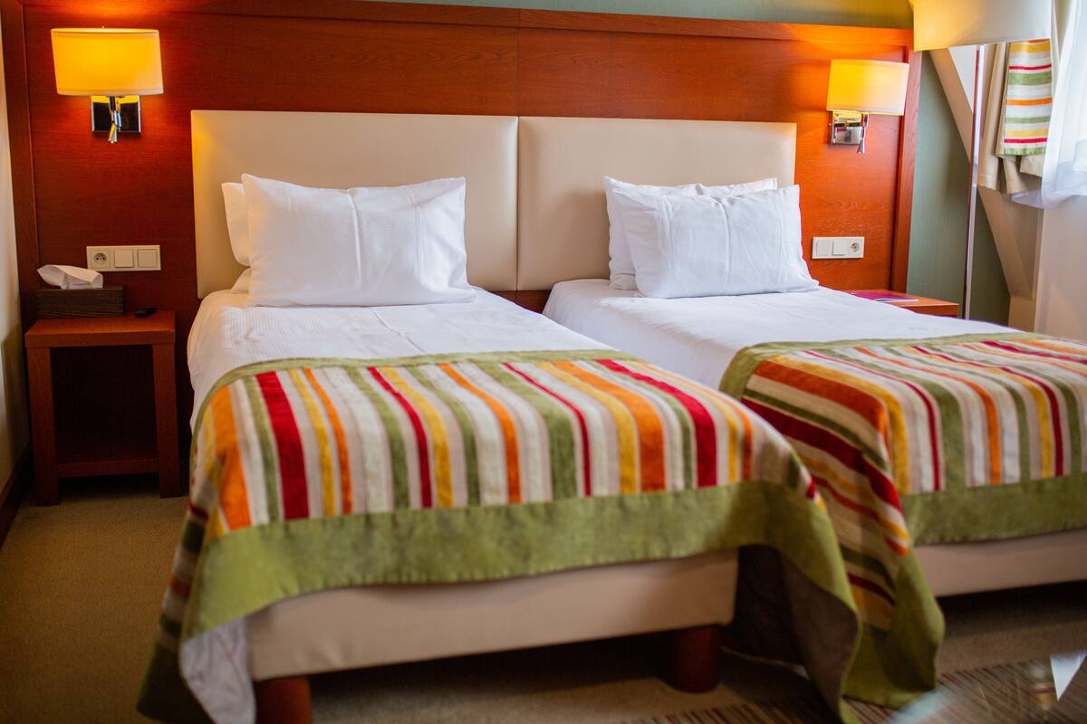 Habitación de hotel con dos camas, cada una con una manta a rayas, un cabecero de madera y una mesita de noche con lámpara.