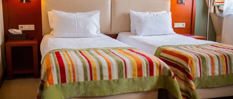 Une chambre d’hôtel avec deux lits, chacun recouvert d’une couverture à rayures, doté d’une tête de lit en bois et agrémenté d’une table de chevet avec une lampe.
