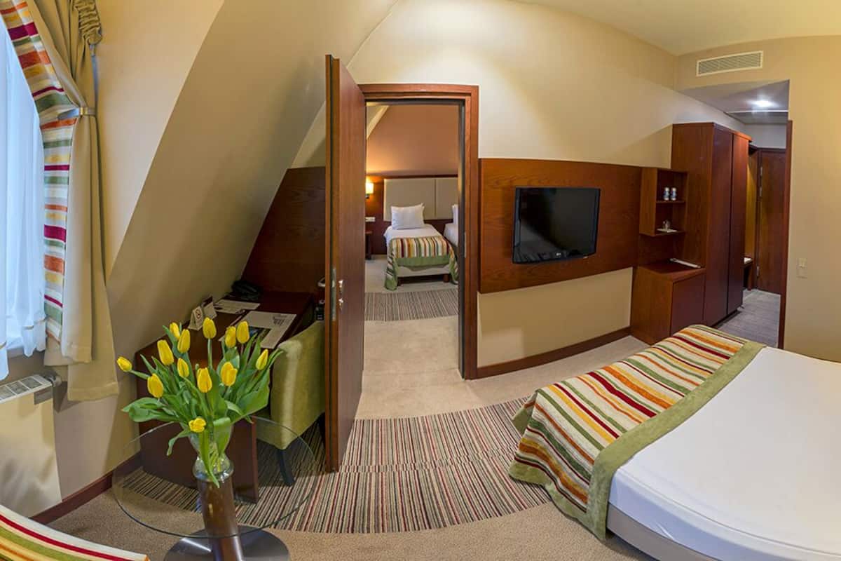 Una habitación de hotel con una cama, televisión, escritorio y un pequeño rincón de descanso.