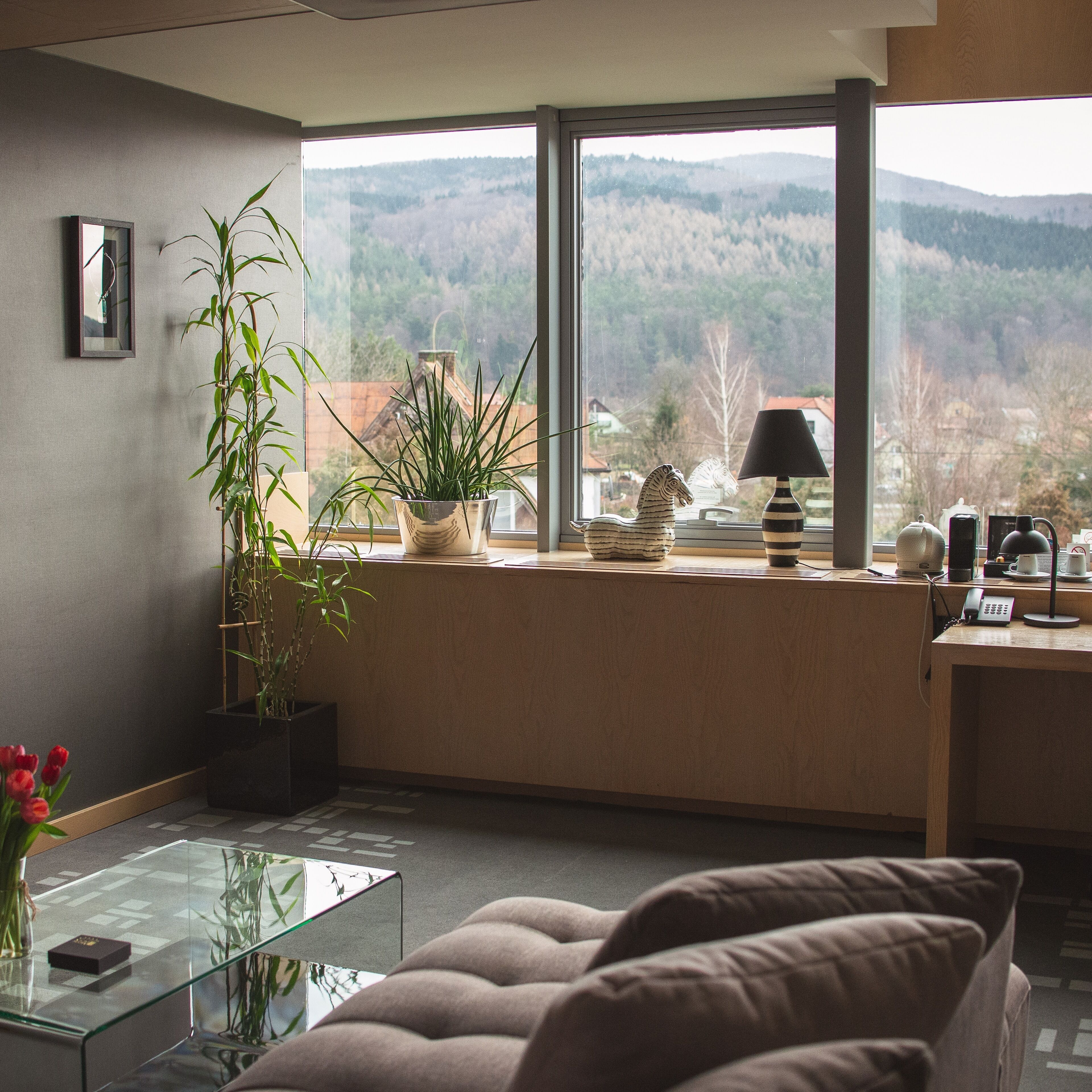 Sala de estar moderna com mesa de centro de vidro, sofá e vista para montanhas através de grandes janelas.